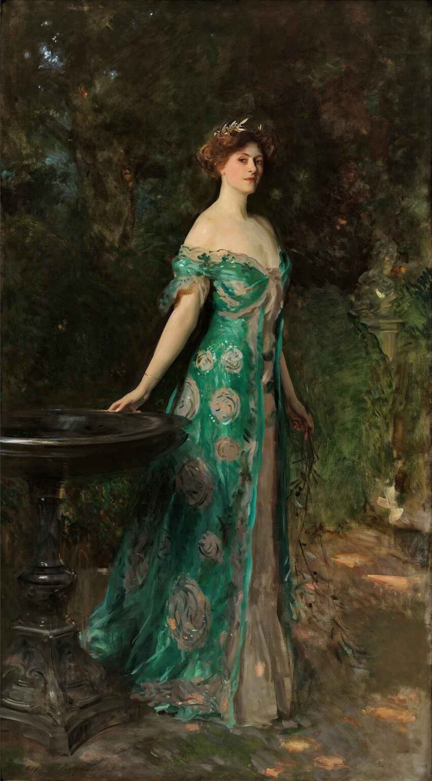 Life-sized portrait of a tall woman in a flowing turquoise gown standing beside a garden table, set against lush dark foliage; she gazes calmly at the viewer, her red-brown hair adorned with jeweled headpiece and her skin illuminated by soft diffused light.