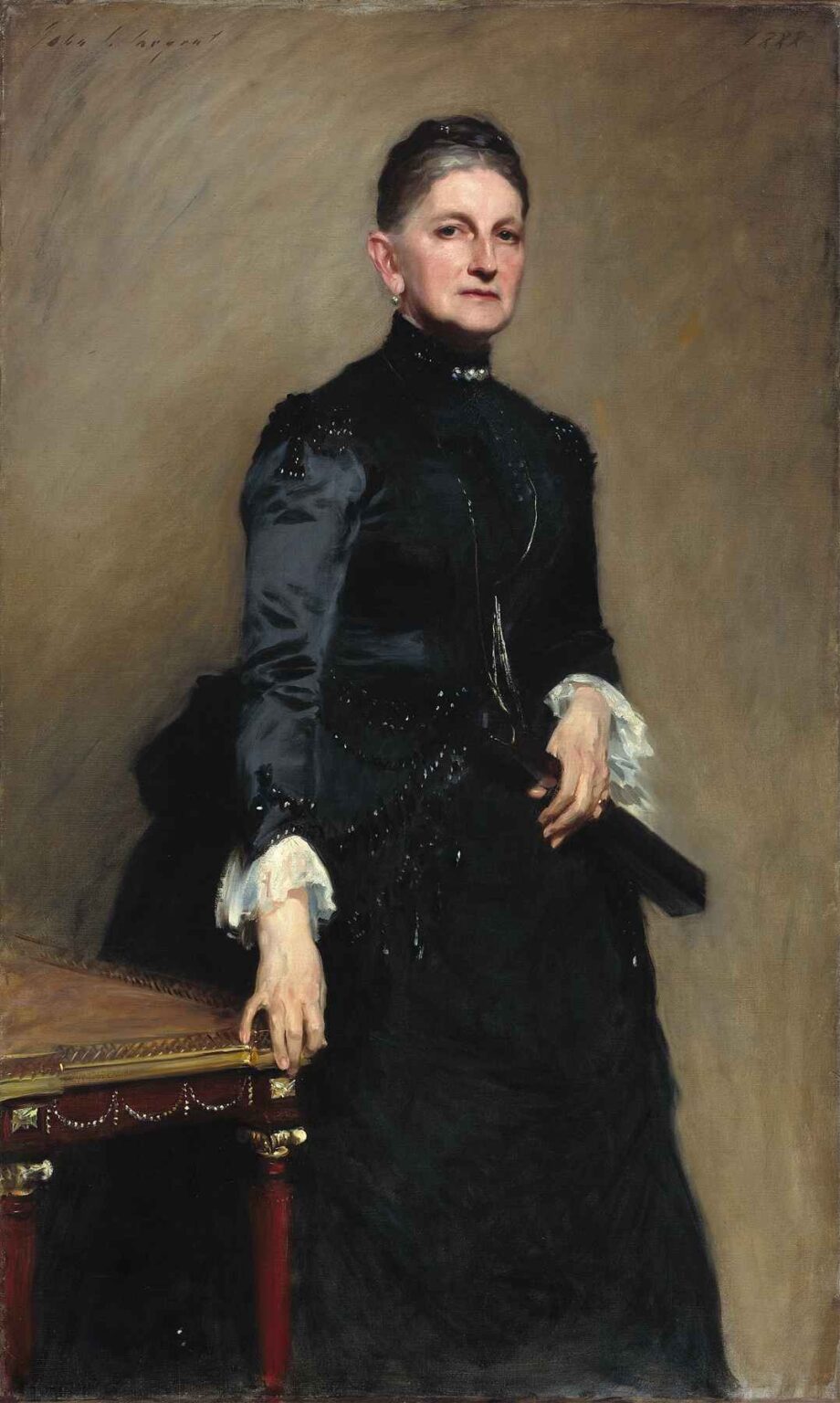 Full‐length portrait of Eleanora O’Donnell Iselin by John Singer Sargent, showing a poised woman in a black gown with lace cuffs, standing beside an ornately carved red and gold table against a neutral backdrop.