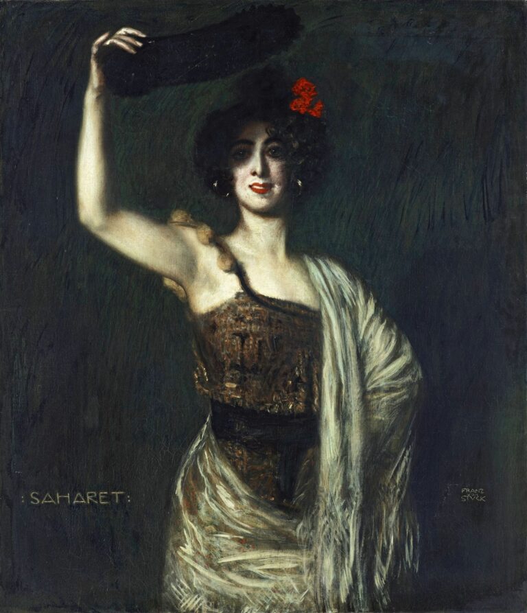 Portrait of dancer Saharet standing in a dark green‑black space, raising a fan above her head, wearing a velvet bodice and ivory fringed shawl, with a red flower in her curly hair.