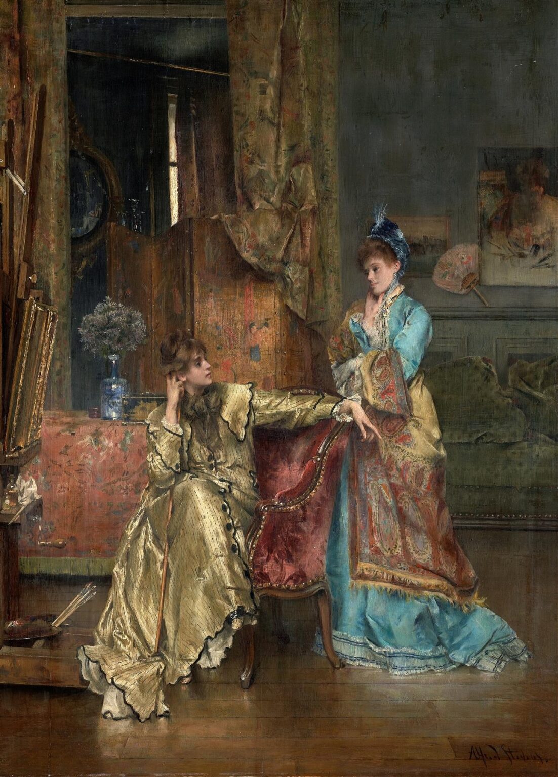 Two elegantly dressed Victorian women—one seated in a gold-trimmed red armchair, the other standing in a blue gown draped with a paisley shawl—engage in a poised exchange amid richly patterned textiles and decorative fans in a 19th‑century salon.