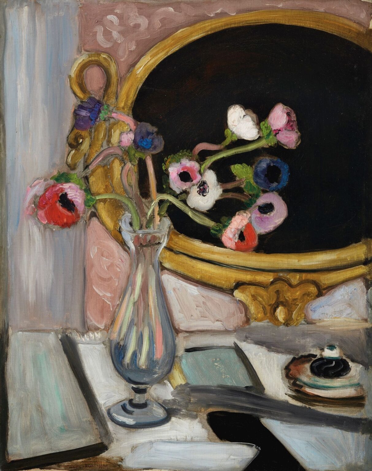 A slim glass vase of pink, red, white, and violet anemones sits on a pale gray-white tabletop beside a small cup and saucer. Behind it, a large oval mirror painted deep black within a gold frame reflects the flowers, set against a rose wall and a vertical blue-gray panel. Oil paint with visible strokes; made by Henri Matisse in 1919.