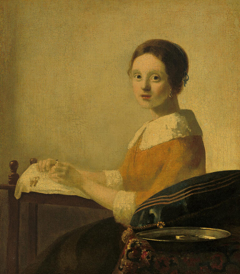 A young woman in a yellow bodice and white collar sits at a table making lace, lit by soft left-side light; a blue sewing cushion and a shallow metal tray rest on a patterned cloth against a plain, warm wall.