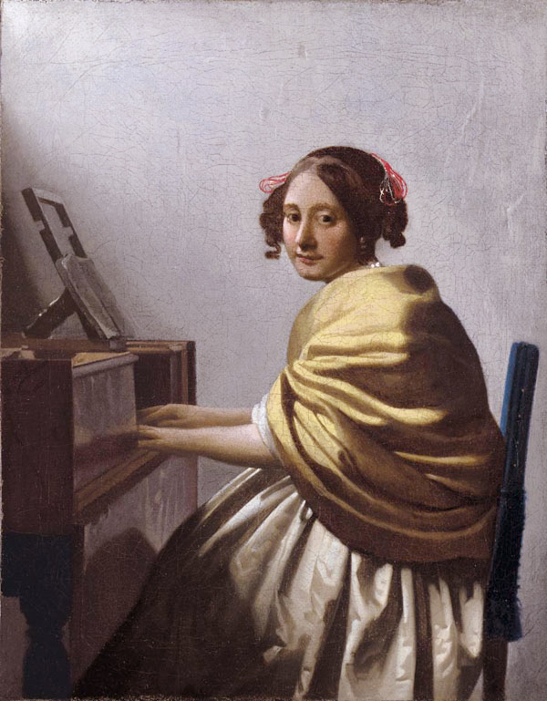 A young woman in a yellow shawl and ivory skirt sits at a virginal, turning to look at the viewer while her hands rest on the keys; pale light washes a simple wall and music stand in a quiet Dutch interior.