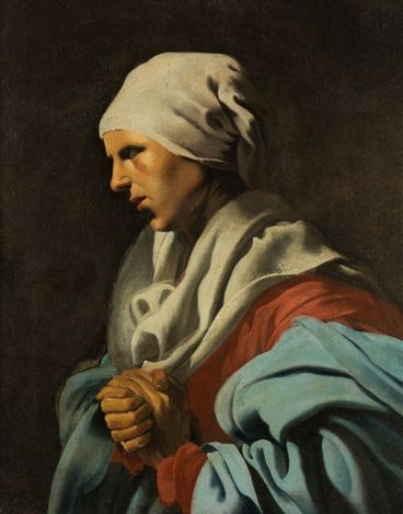 Side-profile of a woman in a white headscarf and blue mantle with hands clasped at her chest, illuminated by a strong left-side light against a dark background.