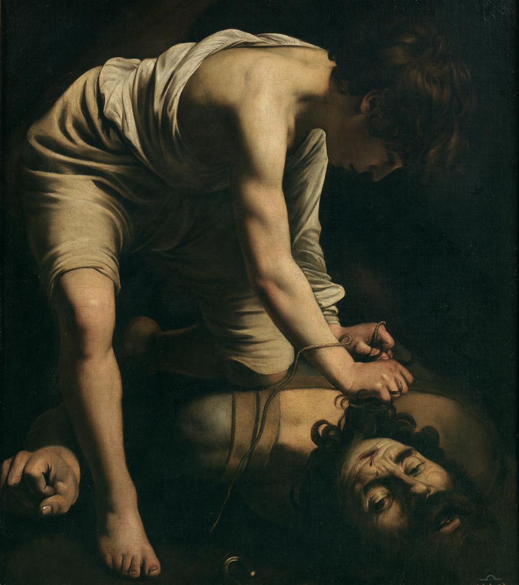 A young David kneels over the fallen Goliath in deep shadow, gripping the giant’s hair as Goliath’s upturned, stunned face fills the lower foreground; raking light illuminates David’s bare shoulder and arms while a sword hilt glints near the giant’s beard.