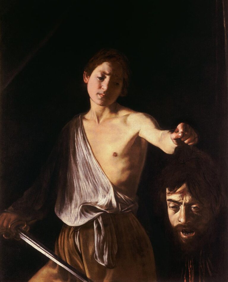 A young David stands against a dark background holding a sword in one hand and the severed head of Goliath by the hair in the other; his face is calm and reflective while the giant’s head hangs in shadow, illuminated by a focused light that models skin and steel.