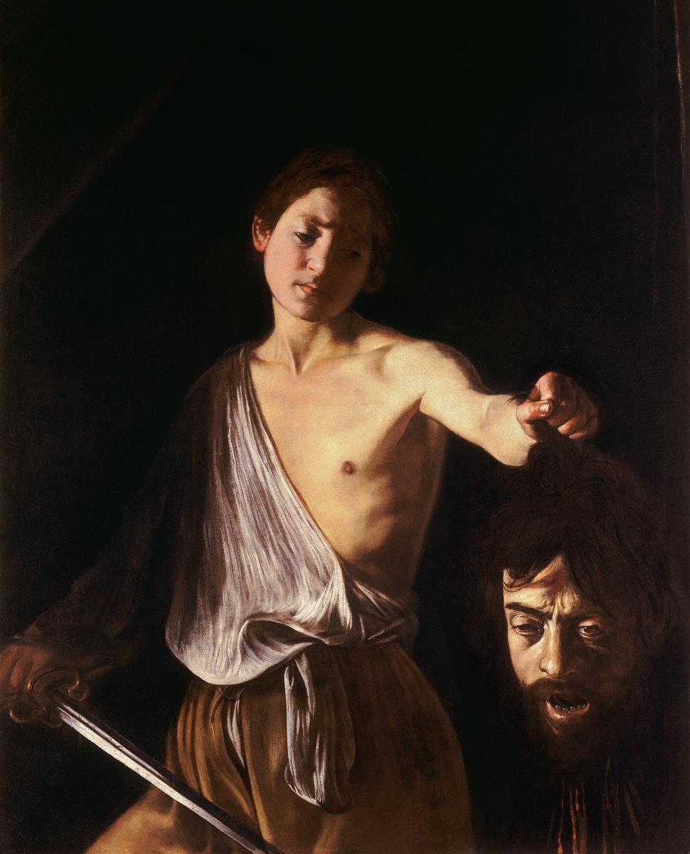 A young David stands against a dark background holding a sword in one hand and the severed head of Goliath by the hair in the other; his face is calm and reflective while the giant’s head hangs in shadow, illuminated by a focused light that models skin and steel.