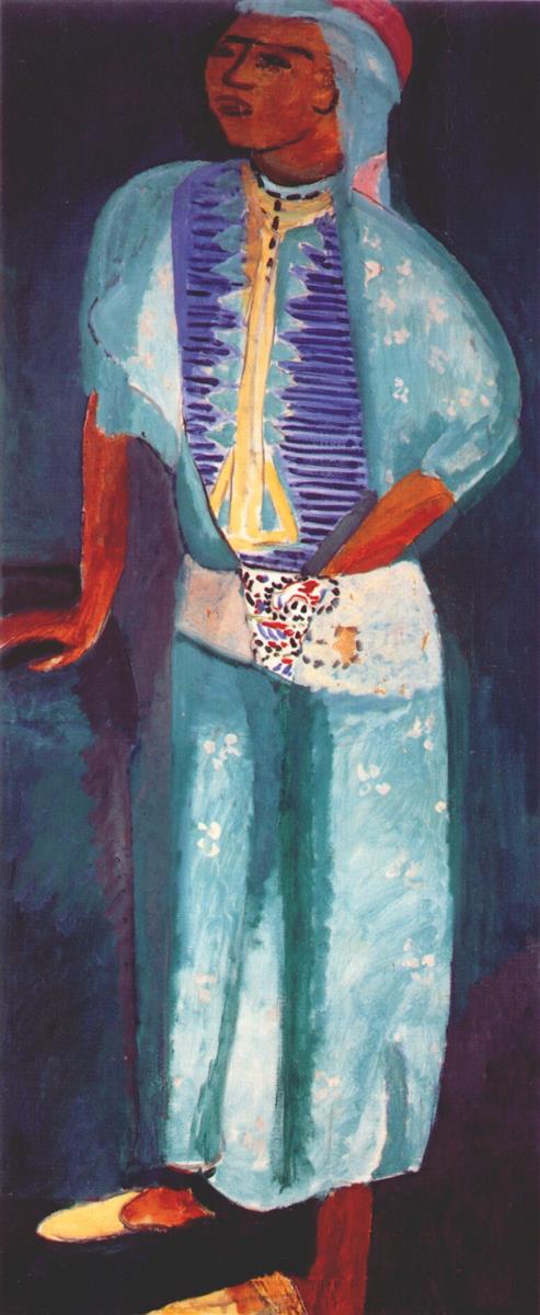 Tall vertical portrait of a woman standing against a dark blue field, wearing a light turquoise robe with small white blossoms, a violet vest with a yellow placket, and a pink head covering; one hand rests on a ledge, the other at a patterned sash; warm ochre skin and simplified features outlined by dark painted contours in Henri Matisse’s 1912 “Fatma.”