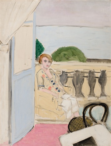 A woman in a pale robe sits at an open blue doorway on a pink-floored balcony, framed by a stone balustrade with green shrubs and a calm sea beyond, while a basket rests in the foreground.