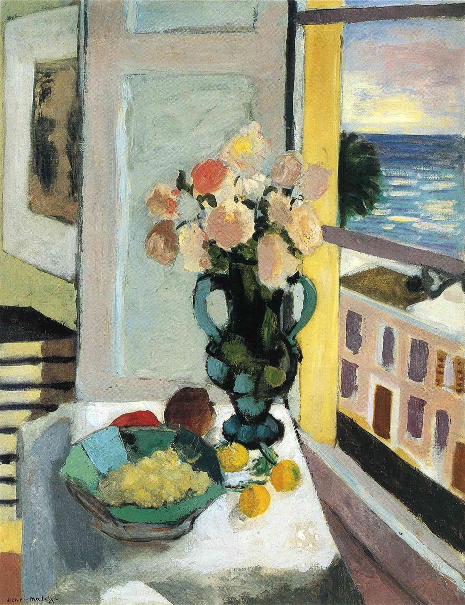 Interior with a white table holding a green-glass vase of pink and cream flowers beside a green bowl of fruit and three lemons; to the right an open window reveals blue sea and sky and a building façade; pale gray paneling and warm yellow jambs frame the view in Matisse’s calm Nice-period palette.