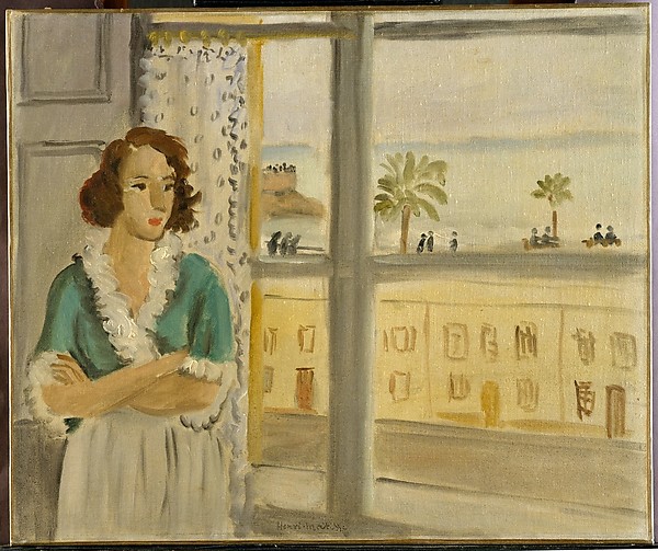 A young woman with red hair stands beside a dotted curtain and tall window, arms folded, while outside a sunlit façade, palm trees, promenaders, and a pale band of sea appear through the panes in Matisse’s soft Nice-period palette.