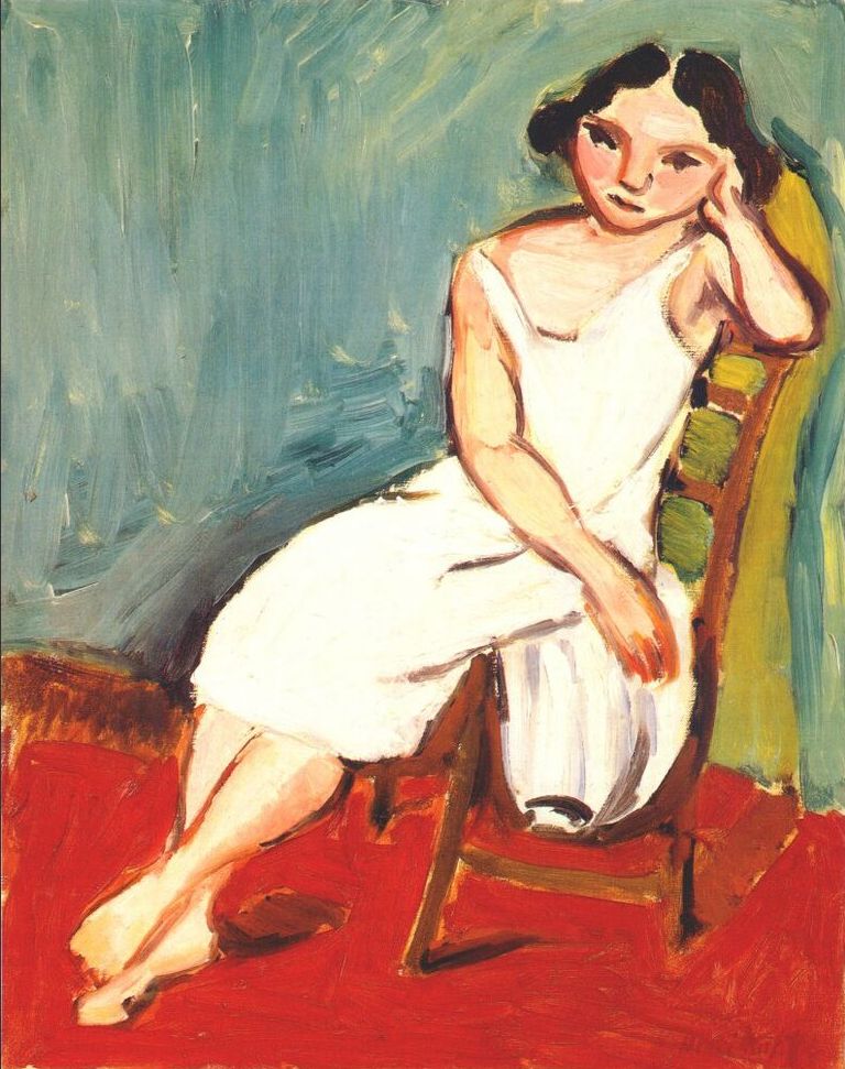 A young woman in a simple white slip sits diagonally on a wooden chair with a green cushion, resting her cheek in her hand; a vivid red floor meets a blue-green wall painted with broad strokes, while bold dark contours define the figure in Matisse’s 1909 “Girl Seated.”