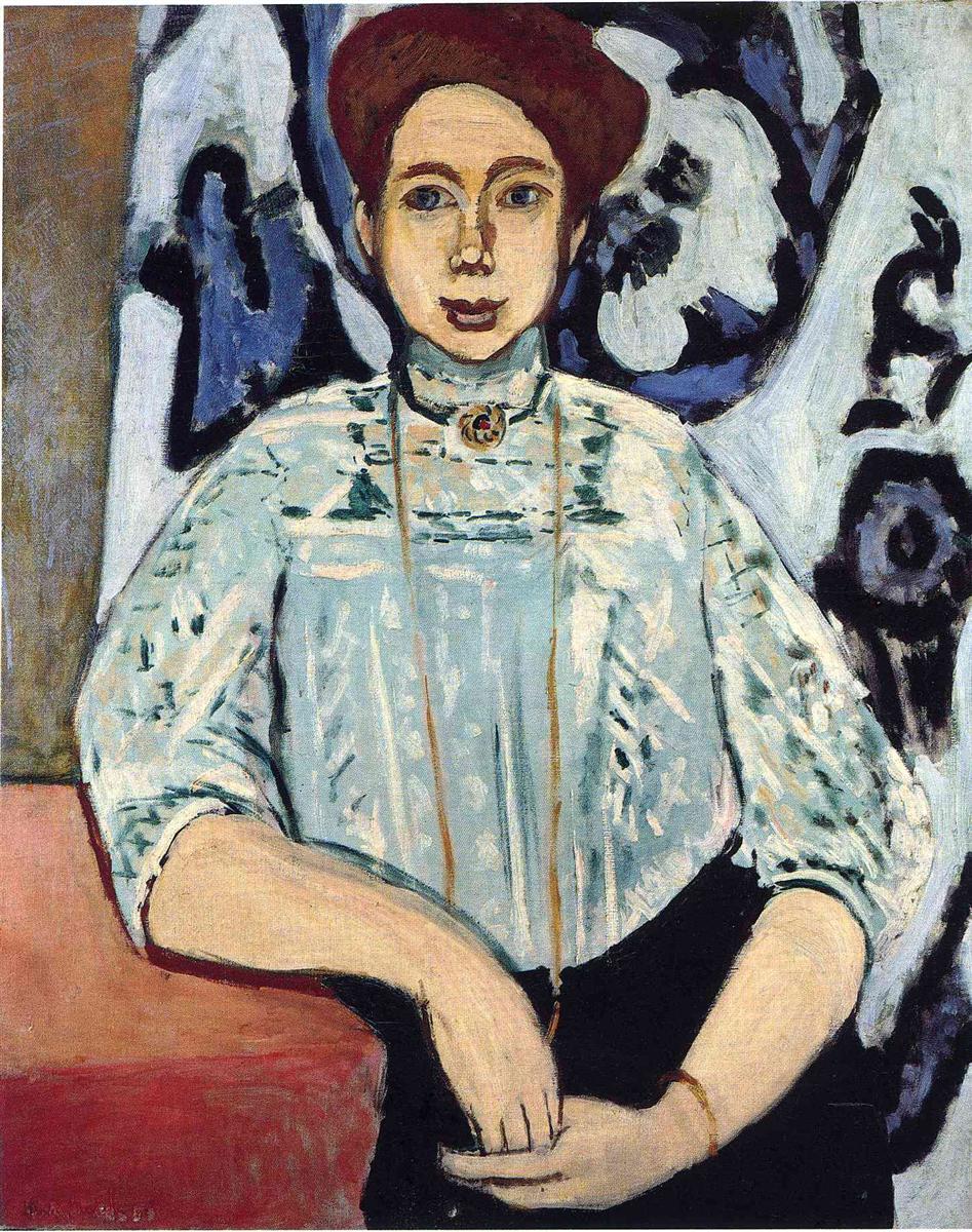 A seated young woman with reddish hair and a pale blue patterned blouse faces the viewer, hands folded at her lap, set against a bold blue-black decorative backdrop; simplified contours and balanced colors convey calm modern poise in Matisse’s 1908 portrait “Greta Moll.”