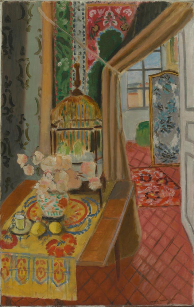 A richly patterned interior shows a table with a yellow runner, vase of pale flowers, lemons, and a small glass; behind it a golden domed birdcage stands beside a pulled-back curtain that reveals a second room with a red rug, blue floral screen, and an open window, all bathed in soft daylight.