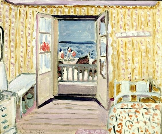 Sunlit hotel room with yellow patterned wallpaper and pale floorboards; open double doors lead to a balcony and blue sea with tiny Bastille Day flags; a white-topped console stands left, a floral bed and headboard at right, all painted in soft creams, violets, and blues.