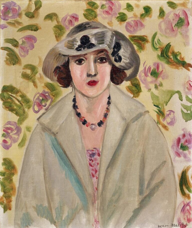 Frontal portrait of a young woman wearing a wide white horsehair hat and pale coat, a bead necklace at her neck, and a glimpse of patterned dress; behind her a cream wall scattered with pink roses and green leaves; soft, even light and restrained colors characteristic of Matisse’s Nice period.