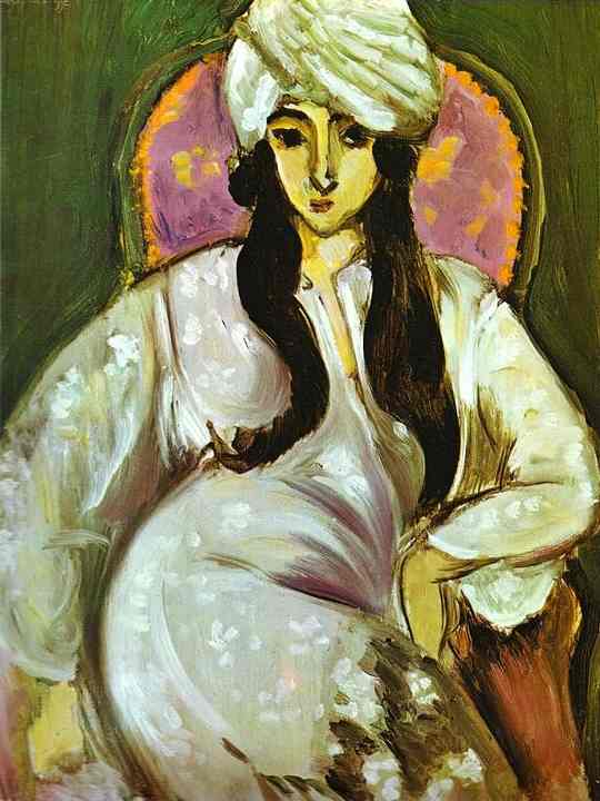 Seated portrait by Henri Matisse of Laurette wearing a white turban and flowing white robe in a pink-backed chair against a deep green background; black contours, long dark tresses, and milky highlights give the 1917 painting a serene, decorative authority.