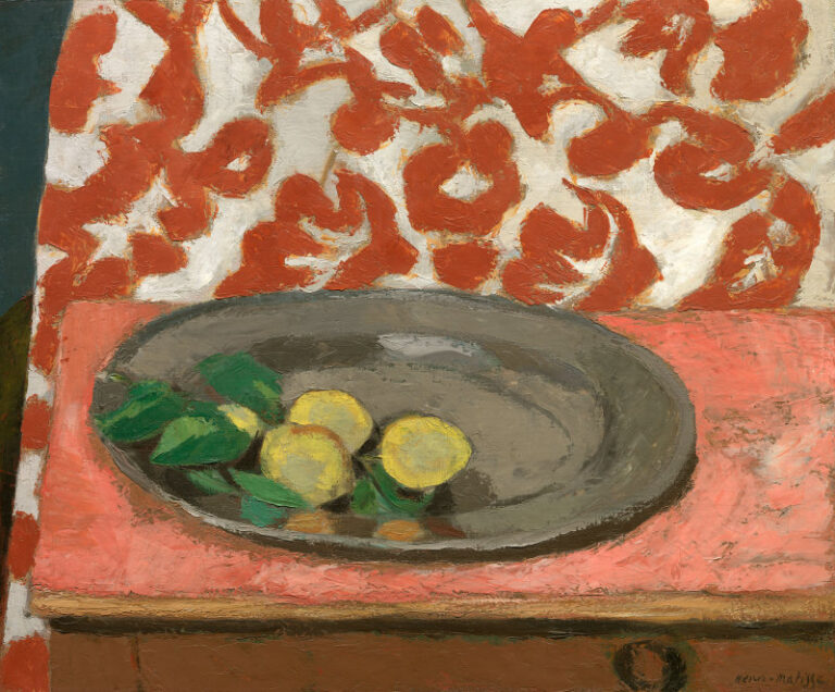 Shallow still life with a large gray pewter oval plate resting on a coral-pink table, three yellow lemons with green leaves inside the dish, and a cream backdrop covered by big rusty-red floral motifs; warm table contrasts with cool metal and lively fruit; Henri Matisse, 1929.