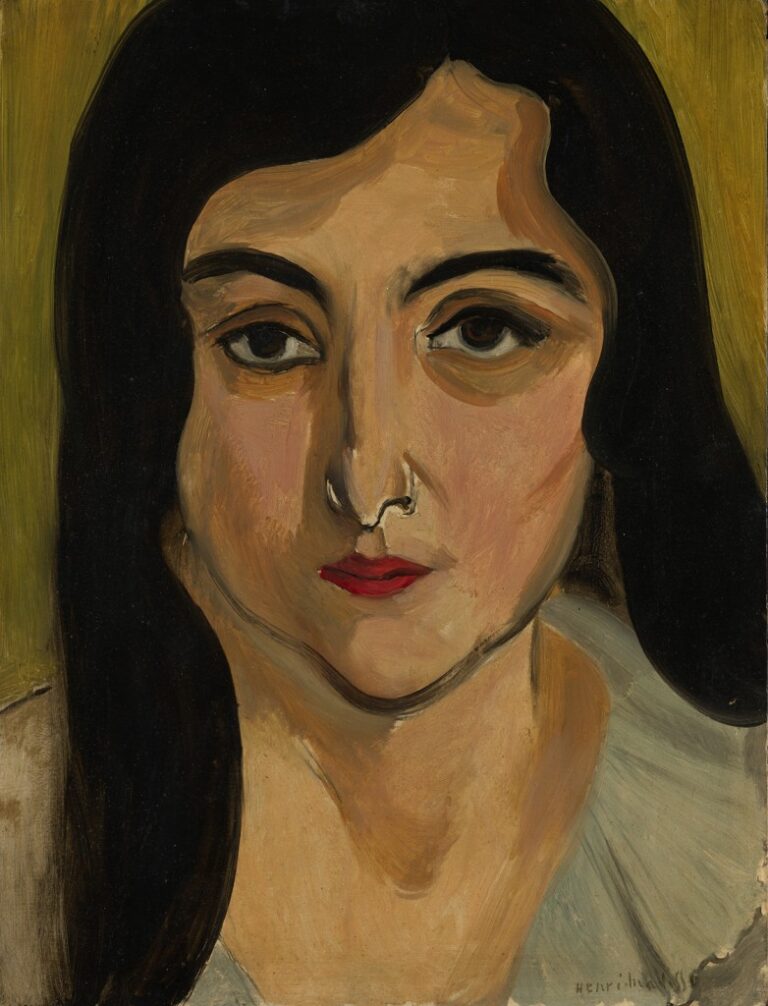 A tightly cropped portrait by Matisse showing Lorette’s head filling the canvas: warm ochre skin, dense black hair framing the face, dark arched brows and soft brown eyes, a narrow highlighted nose, and a small bright-red mouth against an olive background with hints of a pale gray blouse at the shoulders.