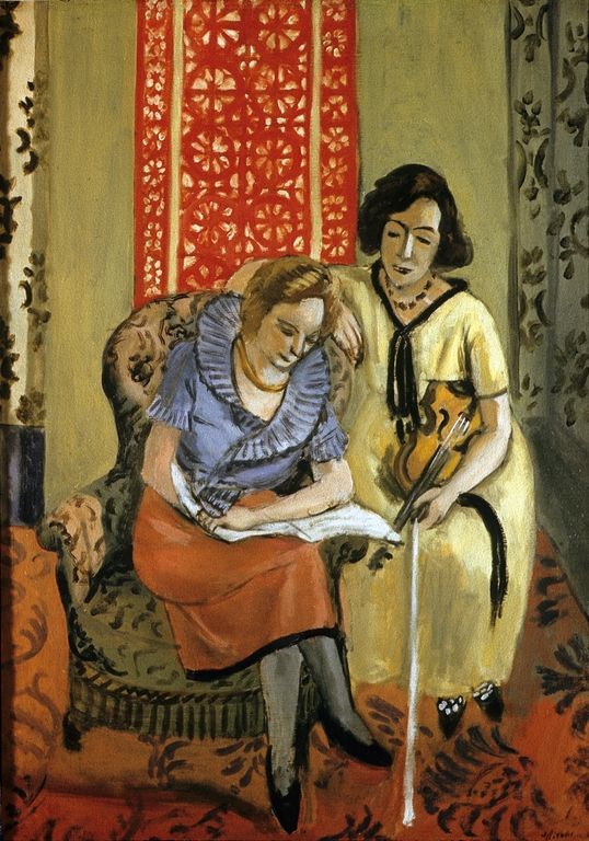 Two women in an upholstered room; one sits reading a music score while the other stands beside her holding a violin and bow, framed by a bright red patterned panel and darker floral drapes over a warm carpet.