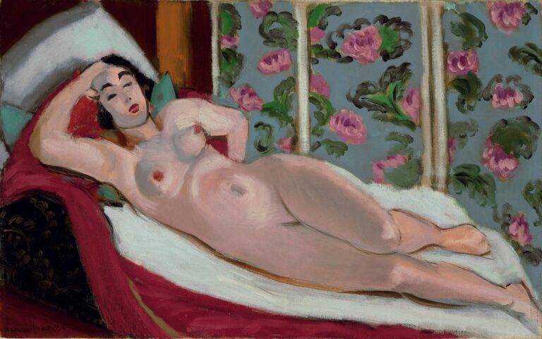 Reclining nude woman stretched diagonally on a chaise with crimson bedding and white sheet, head at upper left on pillows, blue-gray floral screen with pink roses behind, simplified facial features and soft, even Mediterranean light characteristic of Matisse’s Nice period.