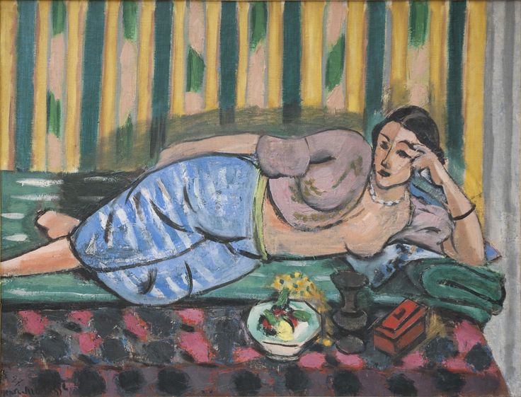 Reclining woman on a green divan with blue trousers and lilac blouse, propped on her hand before a striped yellow-green wall; small red box, dark chalice, and bowl of fruit on a patterned rose-and-black floor; Henri Matisse, 1927.