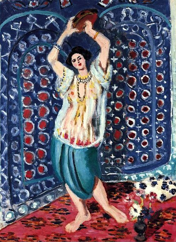 Standing dancer with arms raised holding a tambourine, wearing a sheer blouse and turquoise trousers on a red patterned carpet before a richly patterned blue screen; decorative, shallow interior painted by Henri Matisse in 1926.