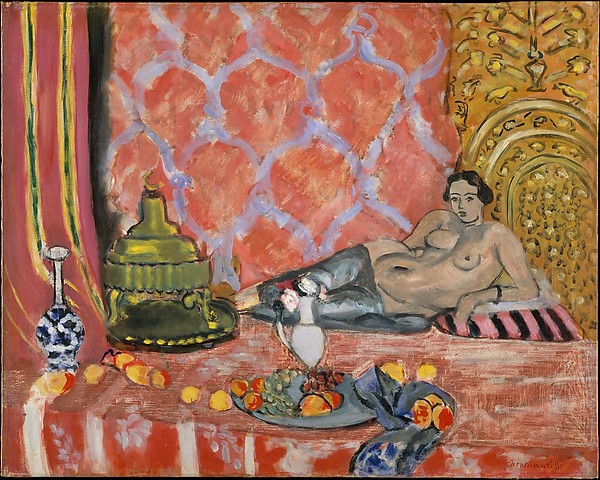 Nude woman reclining on striped cushion wearing gray trousers, before a coral wall with white motifs; green-gold vessel at left, gilded niche at right; foreground table with plate of fruit, lemon garland, blue ribboned napkin, and blue-white bottle; Henri Matisse, 1927.
