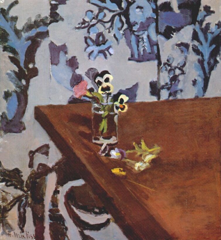 Small bouquet of pansies in a clear glass on a diagonal brown tabletop with a few fallen blossoms; behind, a pale wall covered in indigo and lavender floral pattern; intimate still life painted with warm browns, cool blues, and crisp yellow flower centers.