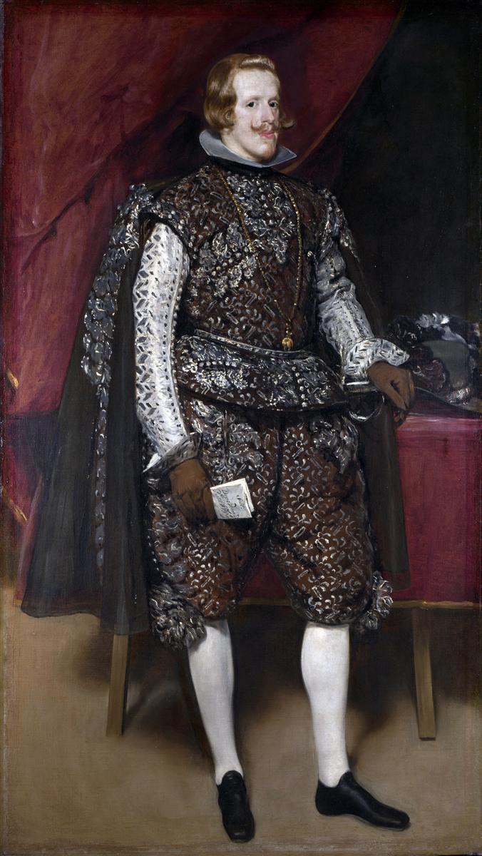 Full-length portrait of Philip IV standing before a red curtain, wearing a shimmering brown suit embroidered with silver, white stockings, and a translucent cape; he holds a folded paper, rests a gloved hand near a sword, and faces the viewer with a composed gaze beside a table topped with a plumed helmet.