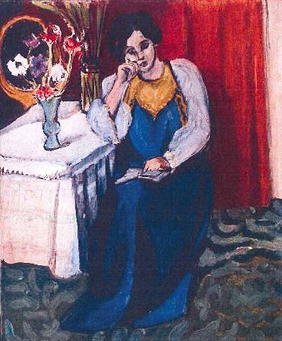 A seated woman in a blue dress with white sleeves and a yellow bodice reads beside a small white-covered table with a vase of flowers and a round mirror; a red curtain hangs behind and a green patterned floor flows beneath, painted with loose, expressive brushwork.