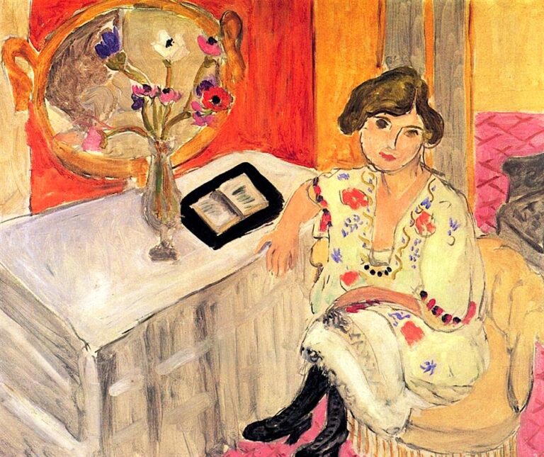 Interior scene of a woman in a pale floral dress seated beside a white-covered table with an open book and a vase of anemones; a round gold mirror, orange and yellow walls, and a pink gridded carpet complete the composition, painted by Henri Matisse.