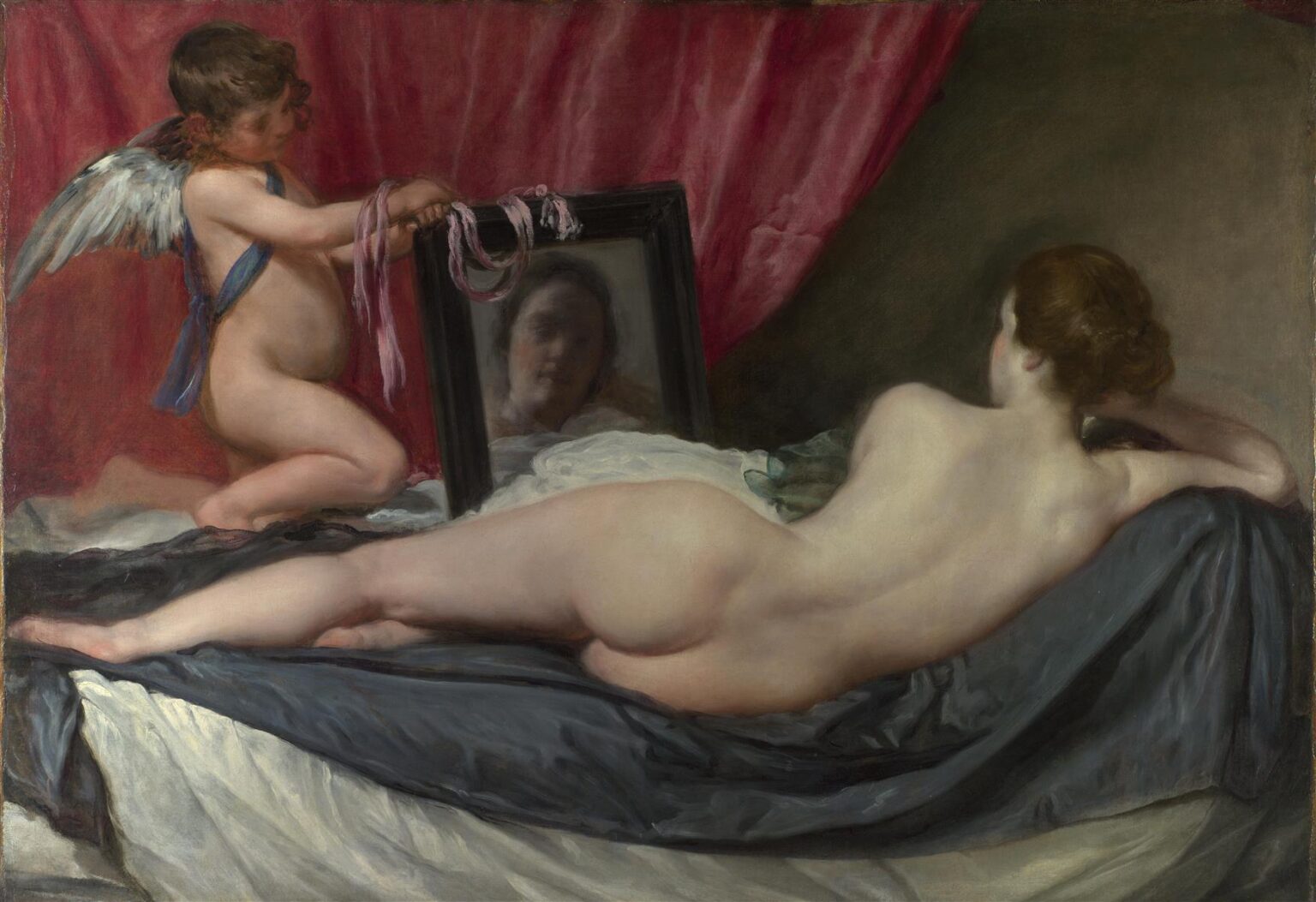 A nude woman reclines on draped fabrics with her back to the viewer while Cupid kneels at the bedside holding a black-framed mirror that shows her soft, blurred face; a crimson curtain and gray bedding frame the intimate scene.