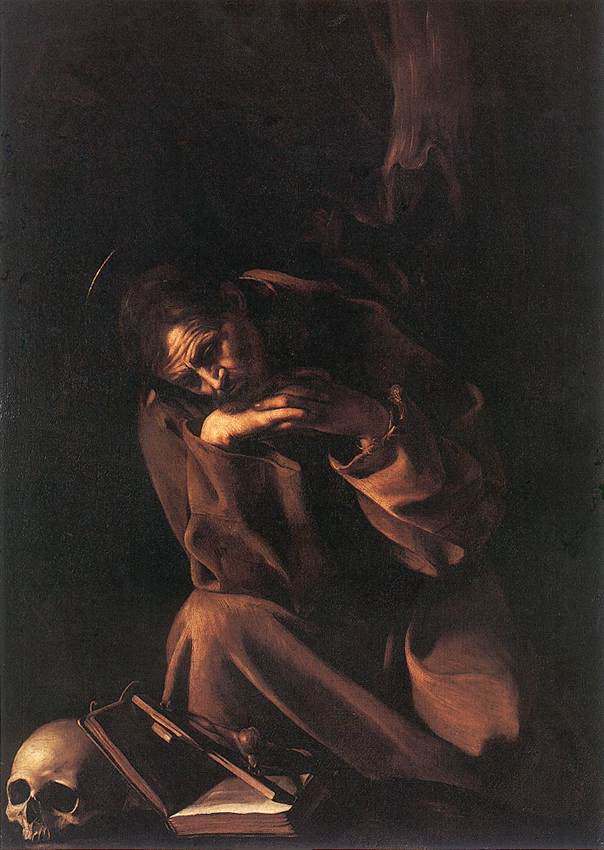 A kneeling Franciscan friar in a brown habit bows his head and folds his arms in deep prayer beside a skull and an open book, all illuminated by a narrow side light against a nearly black background, with a faint halo above his head.