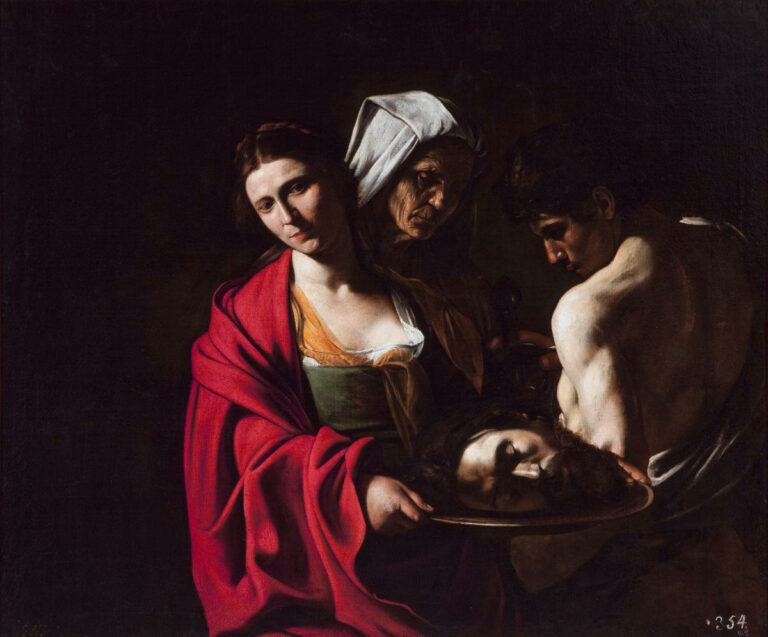 In a dark setting Salome, wrapped in a crimson mantle, holds a platter bearing the severed head of John the Baptist as an elderly woman looks on and the bare-chested executioner lowers the trophy; strong light illuminates their faces and hands against deep shadow.
