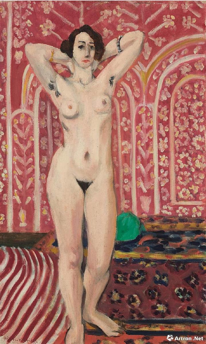 A full-length nude woman stands with arms raised behind her head in a richly patterned pink interior; floral wallpaper and ornate carpets surround her as soft, pale flesh tones contrast with warm reds and a small green accent near her thigh.