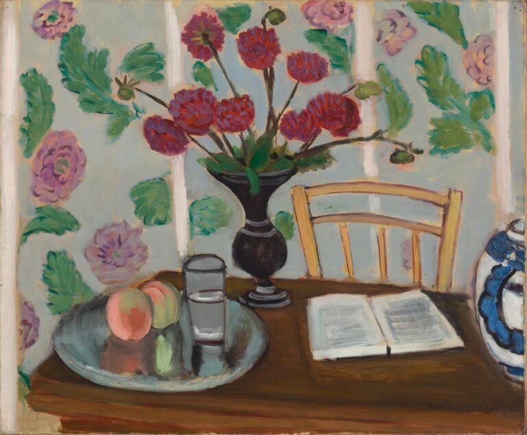 A black vase of red dahlias stands on a wooden table before a pale blue floral wall; at left a silver tray holds two peaches and a water glass, at right an open white book rests beside a yellow chair and a blue-white porcelain jar.
