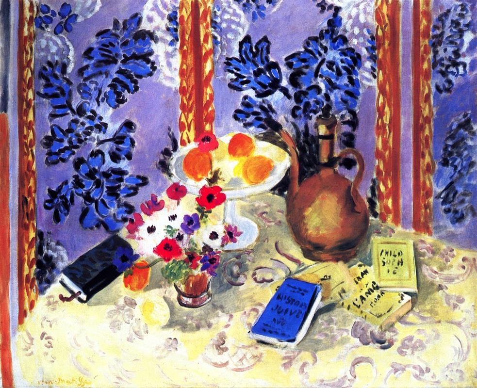 On a cream table patterned with arabesques, a white compote of oranges, a rounded copper ewer, a small bouquet of anemones, and several slim books—one blue titled “Histoires Juives”—sit before a lavender wall covered in dark blue leaves and framed by two golden vertical bands.