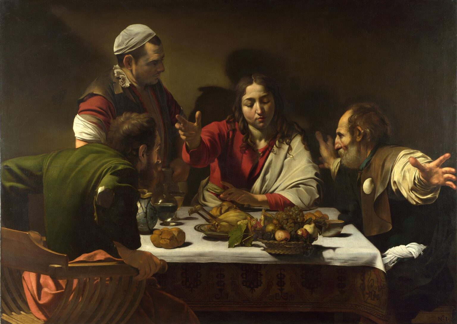 At a table piled with bread, fruit, and roast fowl, Christ raises his hand in blessing as two astonished disciples fling out their arms and a puzzled innkeeper leans in; strong light models faces, hands, and the white tablecloth against a dark room.