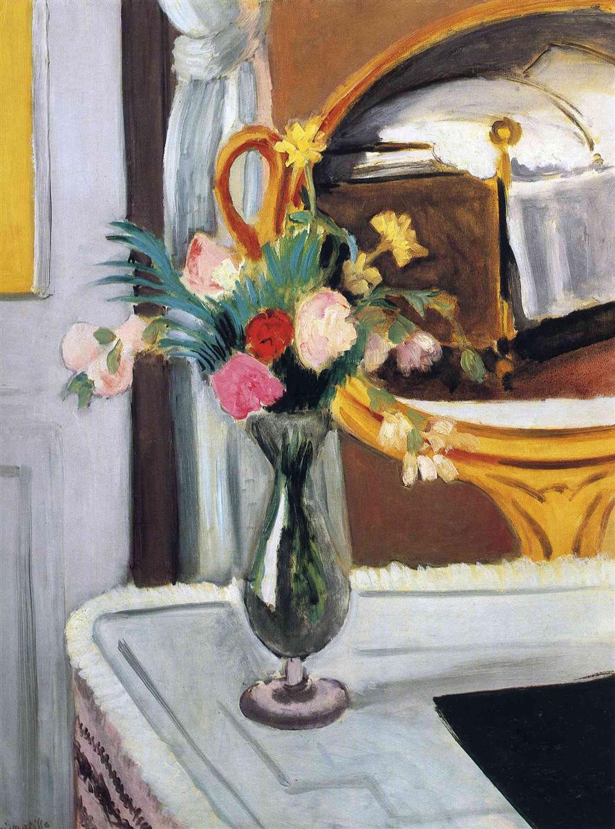 Tall green glass vase of mixed flowers on a pale tabletop before a gold-framed oval mirror reflecting a white-covered bed with brass finial; soft gray door and white curtain at left, small strip of yellow wall, and a dark rectangular object on the table; painted with cool blues, warm ochres, and vivid floral accents.