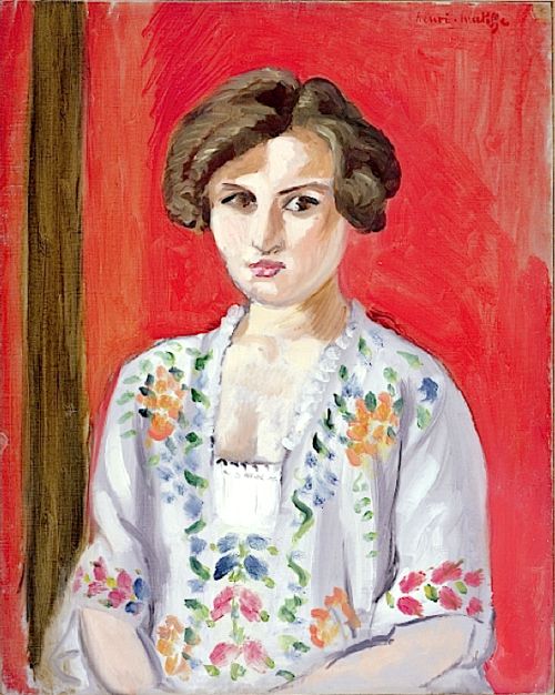 Frontal portrait of a young woman against a vivid red background, wearing a white blouse embroidered with colorful floral sprays; short brown hair frames a steady face, and a vertical brown strip at left balances the composition.