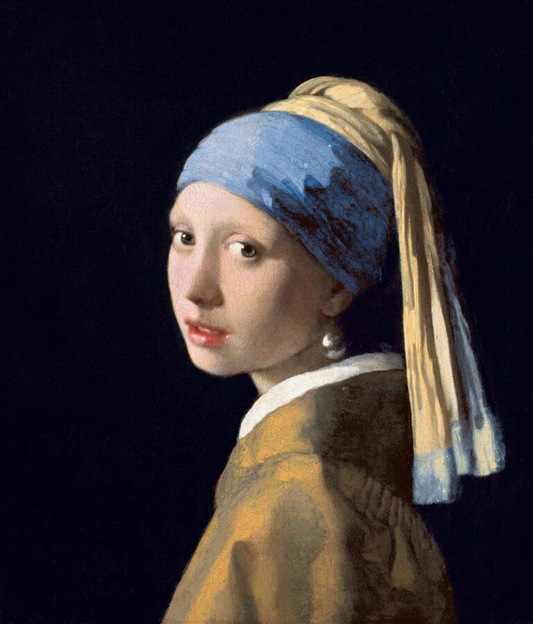 A young woman in a blue-and-ochre turban turns her head over her shoulder toward the viewer; soft light models her face, a large teardrop pearl gleams at her ear, and a dark background isolates the figure.