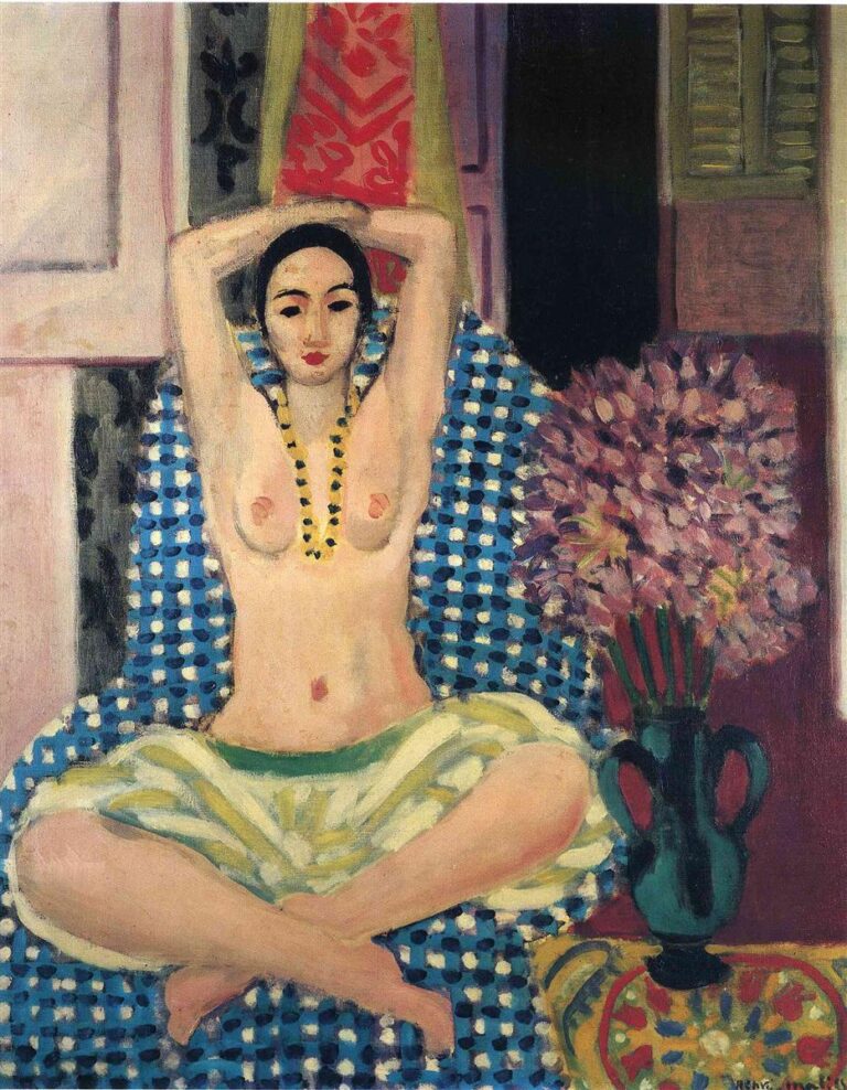 A topless woman sits cross-legged with arms raised behind her head on a blue-and-white checked cloth; red and pink hangings rise behind her, while a turquoise vase with a dense purple bouquet stands at right, all in a shallow, warmly lit interior.