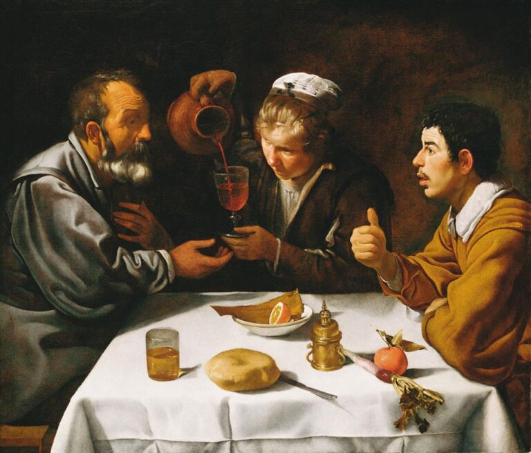 Three figures at a white-clothed table as a server pours red wine into a glass, with bread, citrus, a metal vessel, and vegetables illuminated against a dark background in Velazquez’s “The Lunch” (1620).