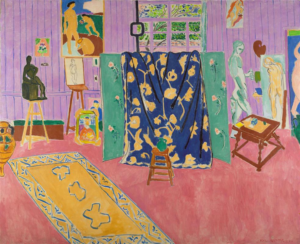 Large interior with a pink floor and lavender wallboards; at center a dark blue floral curtain hangs between two green screens; a yellow-bordered carpet runs diagonally at left; easels, a black bronze on a stool, a small table, a low stool with a green jug, and framed paintings and drawings populate the room; a small window with green foliage appears above, all rendered in flat, saturated color in Henri Matisse’s 1911 “The Pink Studio.”