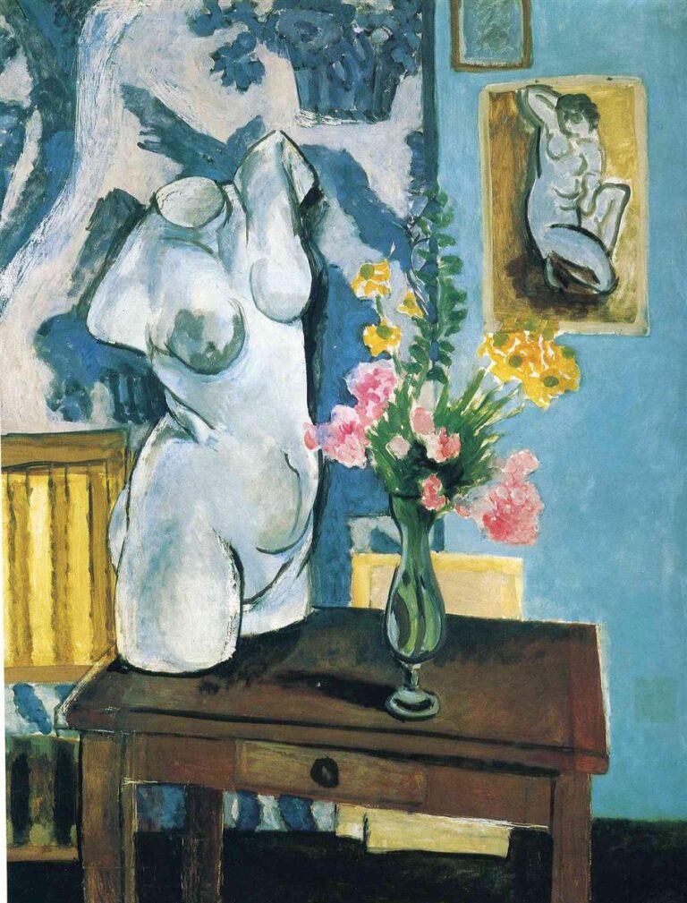 Studio interior with a headless white plaster torso on a dark wooden table; tall green glass vase holding pink and yellow flowers to the right; patterned blue-and-white wall on the left and plain blue wall with small framed reliefs on the right; warm ocher plaque of a kneeling nude echoes the cast; cool Mediterranean light unifies the scene.