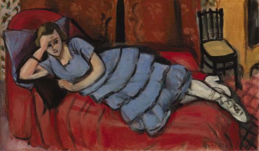 A woman in a blue tiered dress reclines across a vivid red sofa before a warm patterned wall; white stockings and shoes point toward a small black chair at right, all drawn with Matisse’s bold contour and balanced color.
