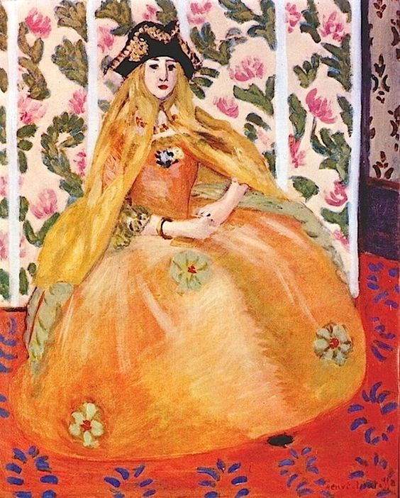 Front-facing woman in a voluminous orange gown with green rosettes and a saffron mantle, wearing a dark tricorn-like hat; seated against vertical panels of cream and floral wallpaper on a red patterned carpet; bright, simplified colors and bold shapes typical of Matisse’s Nice-period interiors.