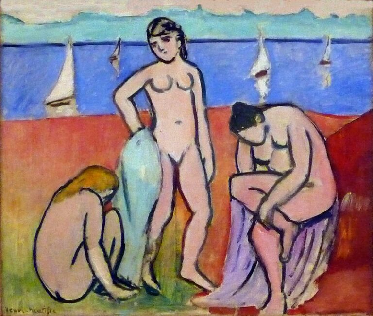 Three nude women on a red beach before a blue sea with white sailboats; one crouches, one stands with a drape, and one sits bending forward, all outlined by dark contours in Matisse’s 1907 style.