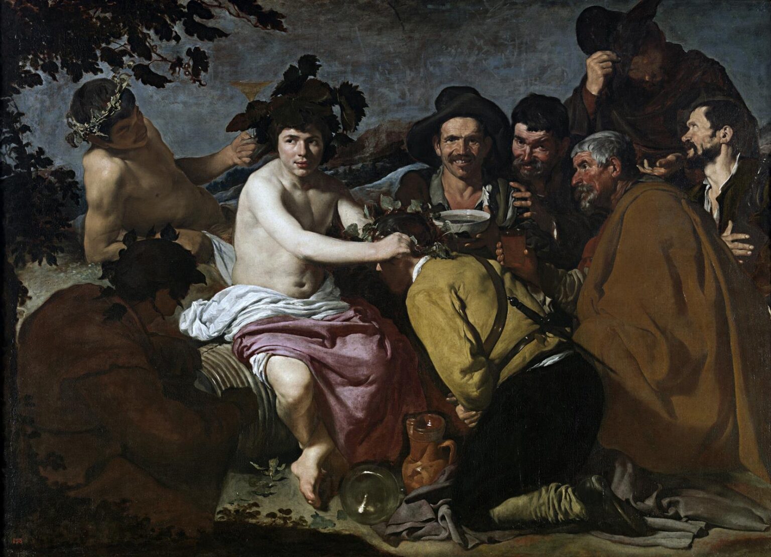 Bacchus sits half-draped on a cask outdoors, placing a vine crown on a kneeling man while a circle of rustic drinkers laugh and raise cups; glass, jug, and leaves lie on the ground under a pale sky in Velazquez’s “Triumph of Bacchus.”